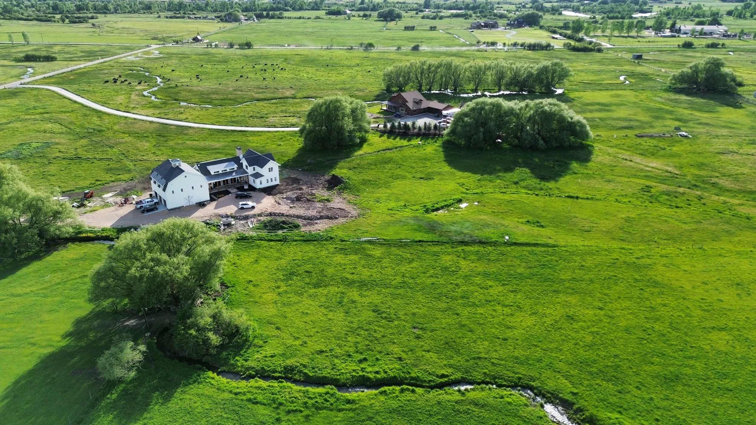 Aerial view of a rural farm with white barn and house surrounded by lush green fields, trees, and small streams.