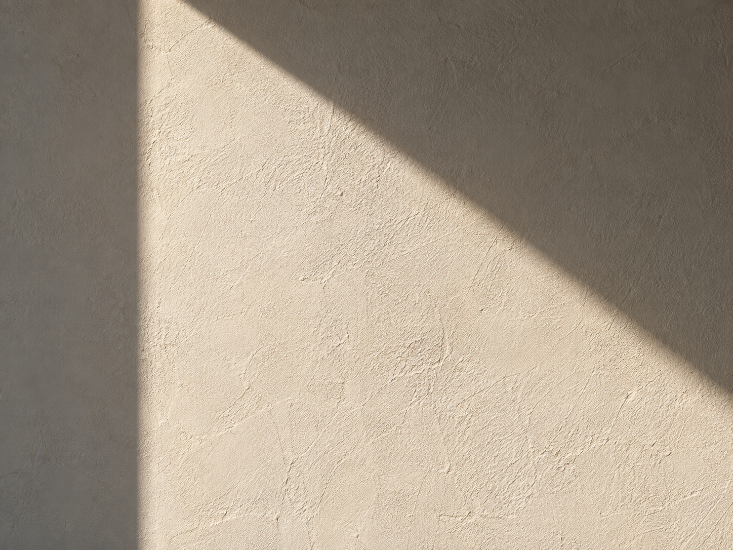 A beige textured wall with a shadow cast across it from the sunlight.