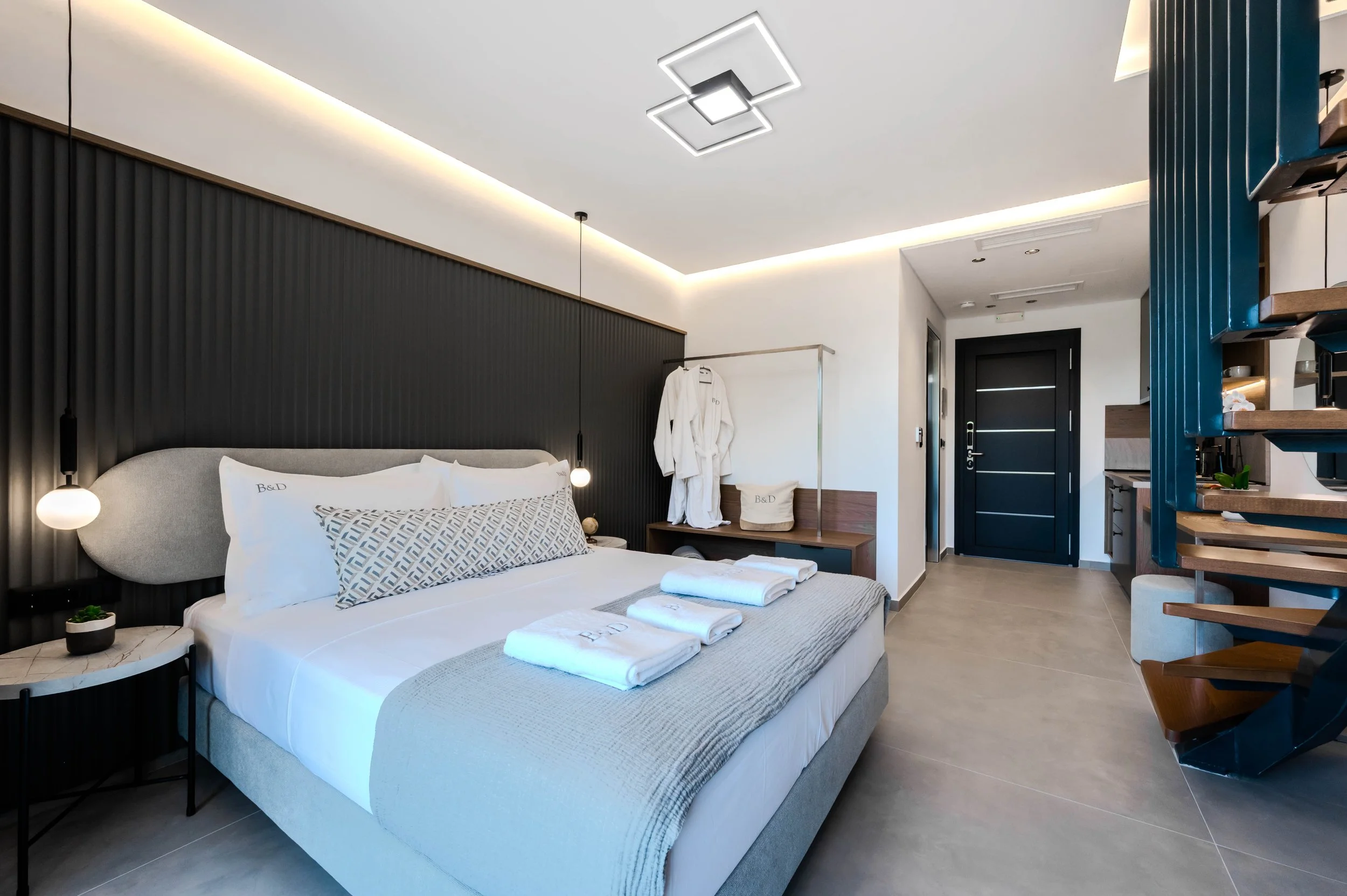 Modern hotel room with a bed, bedside tables, and towels, featuring a dark accent wall and contemporary lighting.