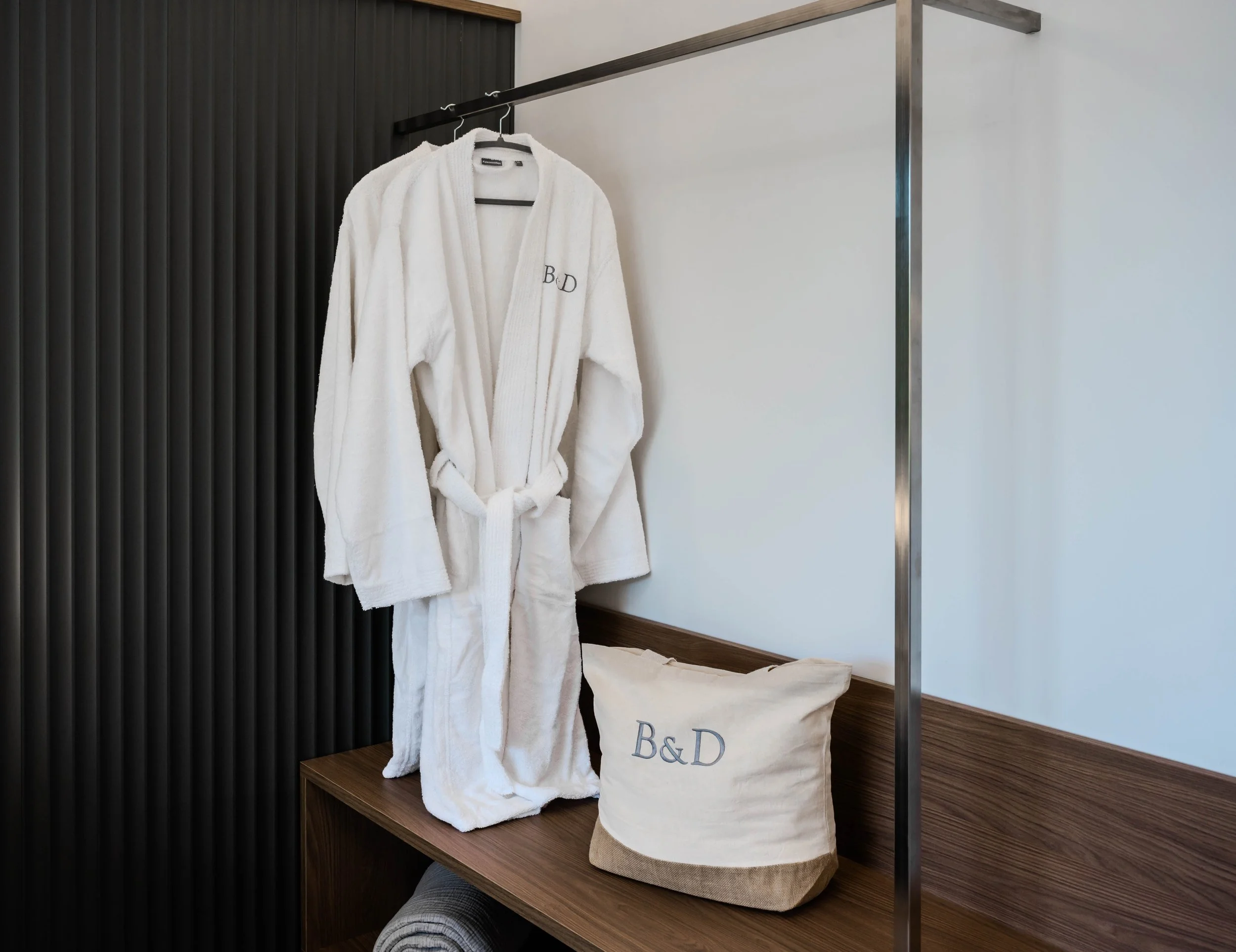 White bathrobe and a cloth bag with the initials 'B&D' on a wooden shelf in a room.