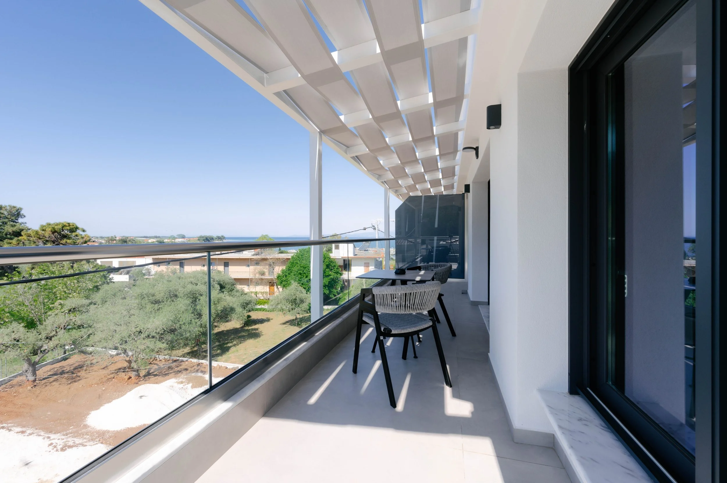 Balcony with seating area, glass railing, white directional canopy, and ocean view in the distance.