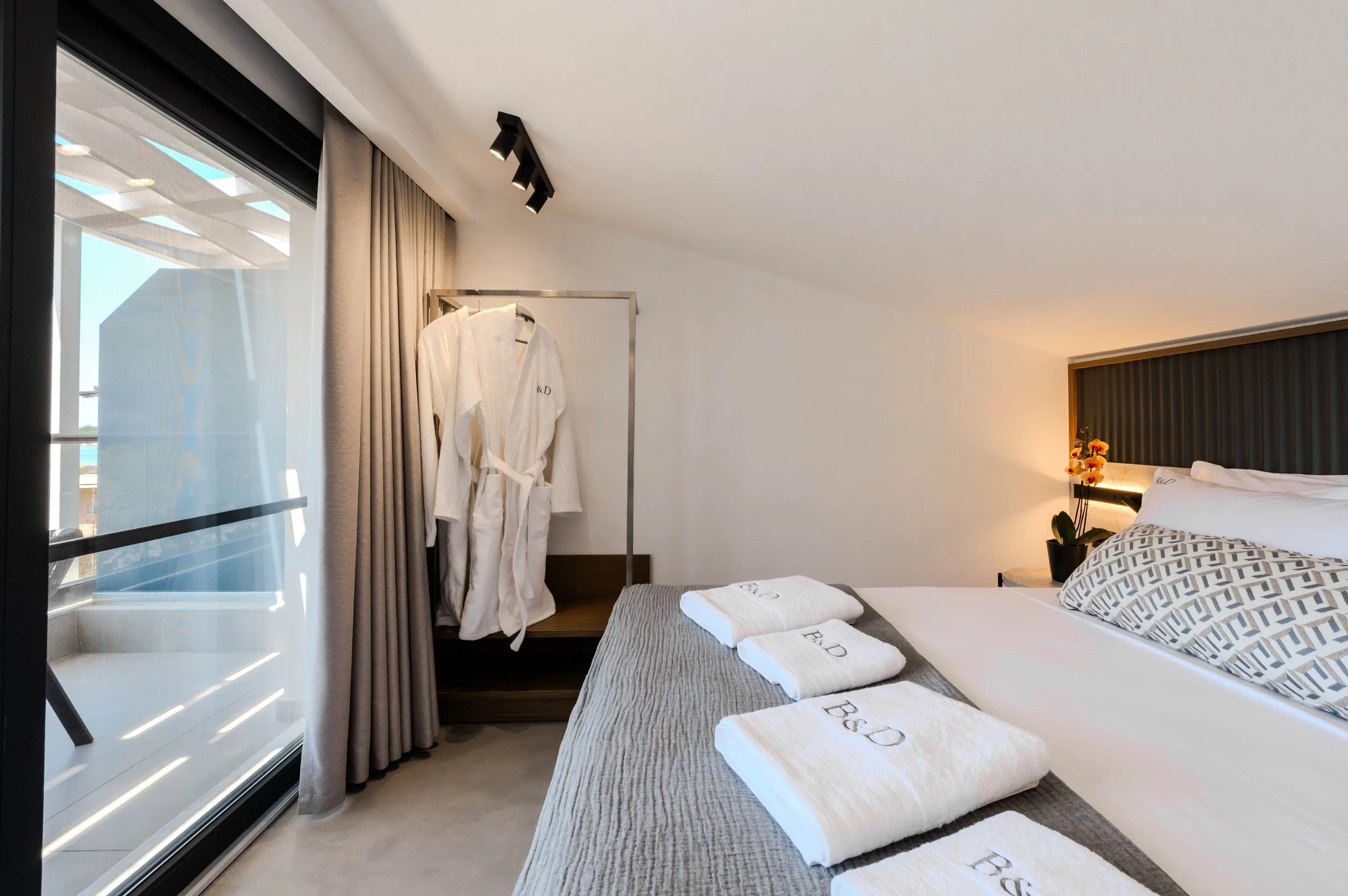 Hotel room with a bed, towels, a robe, and a window with curtains and a balcony view.