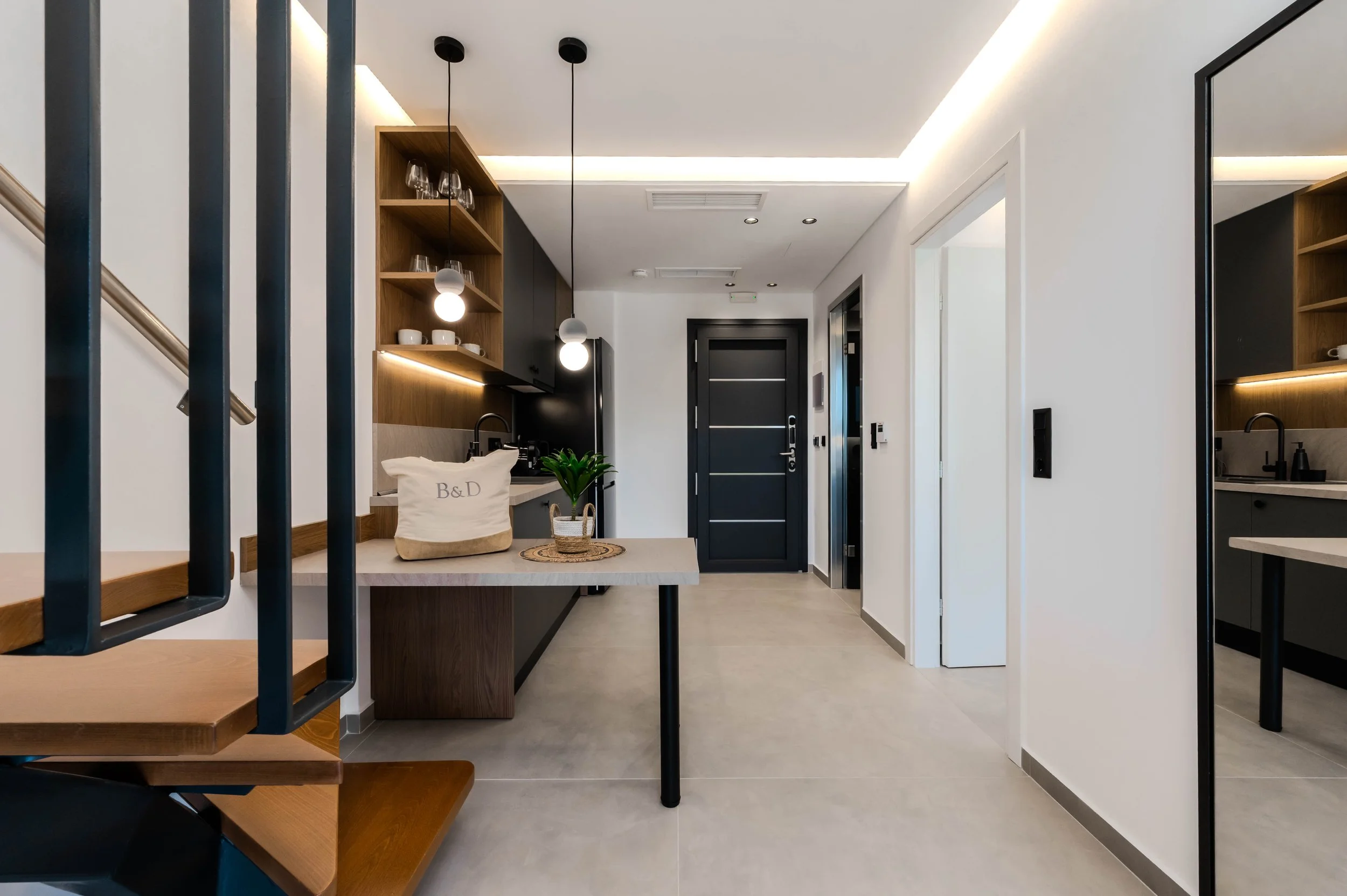 Modern apartment interior with a small kitchen area, black front door, and mirror.
