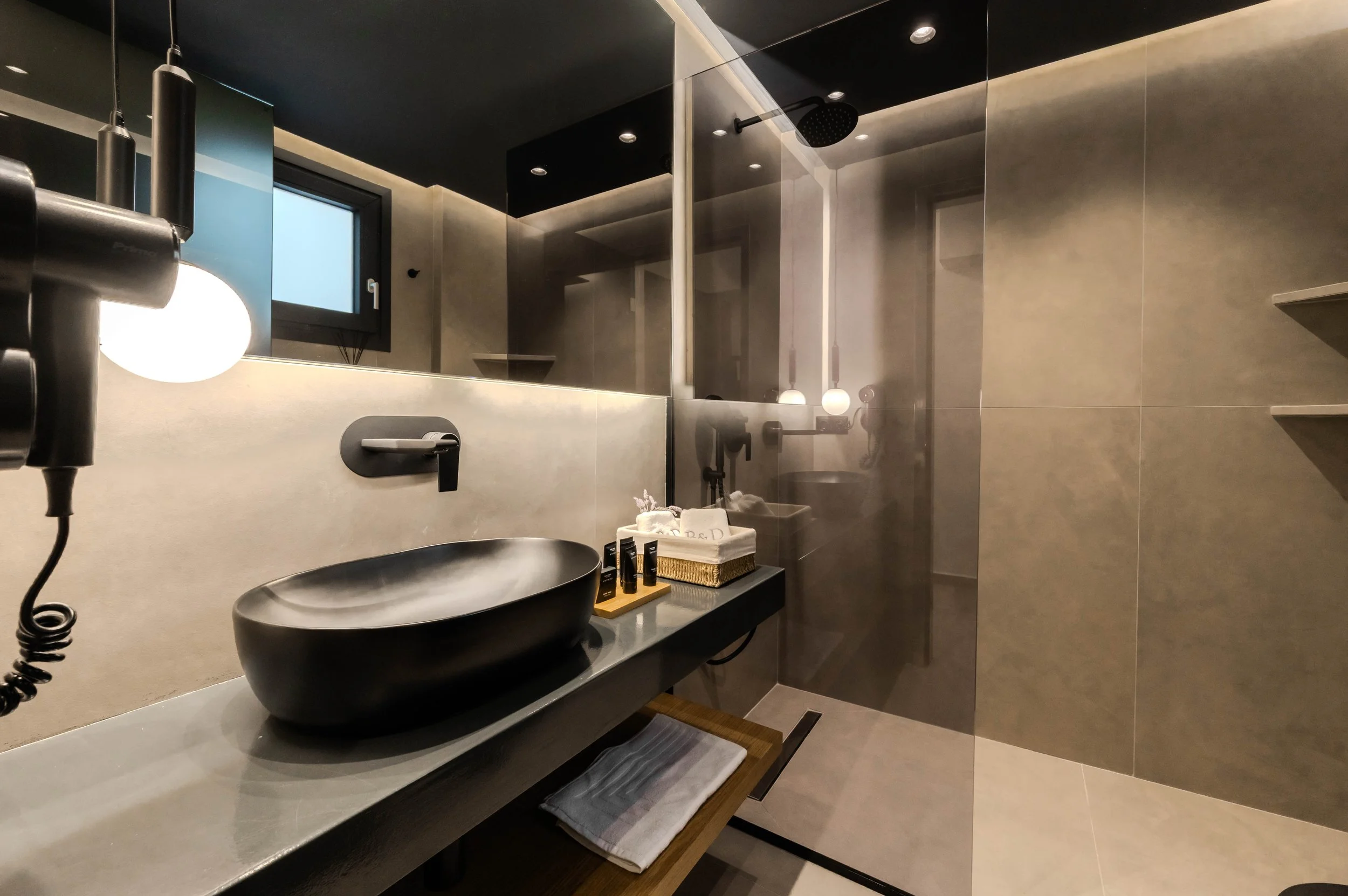 Modern bathroom with a black vessel sink, wall-mounted faucet, large mirror, and a glass shower enclosure with rain showerhead; small window and shelf with toiletries.