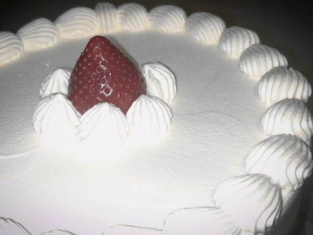 A white frosted cake with a single strawberry and white whipped cream dollops around the edge.