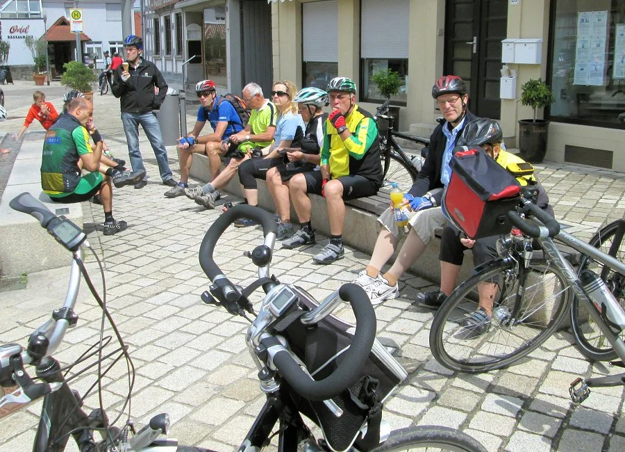 Eine Gruppe von Radfahrern, einige sitzen auf einer Bank und andere stehen neben ihren Fahrrädern, während sie eine Pause in einer Stadt machen.
