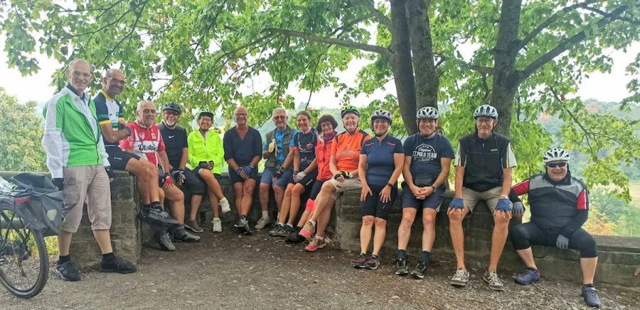Gruppe von Radfahrern, die auf einer Parkbank unter einem Baum sitzen und posieren.