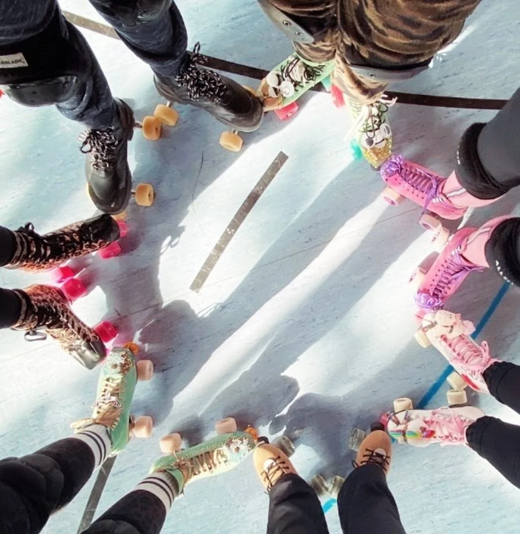 Gruppierung von Menschen auf Rollschuhen im Kreis auf einer Eislaufbahn, die Füße und Rollschuhe sind sichtbar, das Bild wurde von oben aufgenommen.