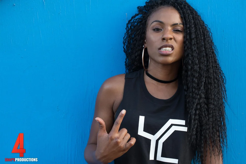 Portrait of a woman with long locs in front of a bright blue wall