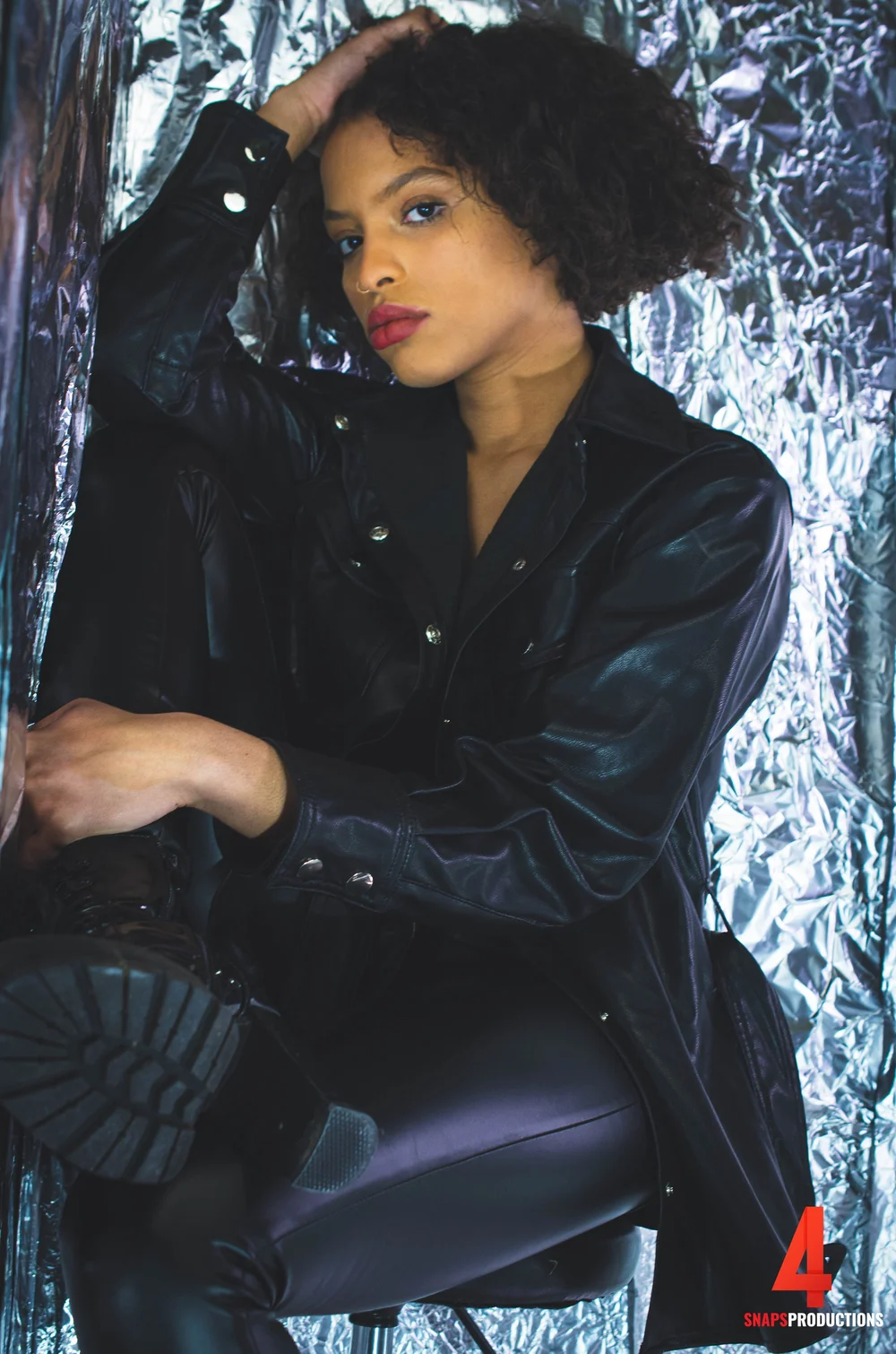 Editorial portrait of a woman in a black leather jacket against a silver backdrop