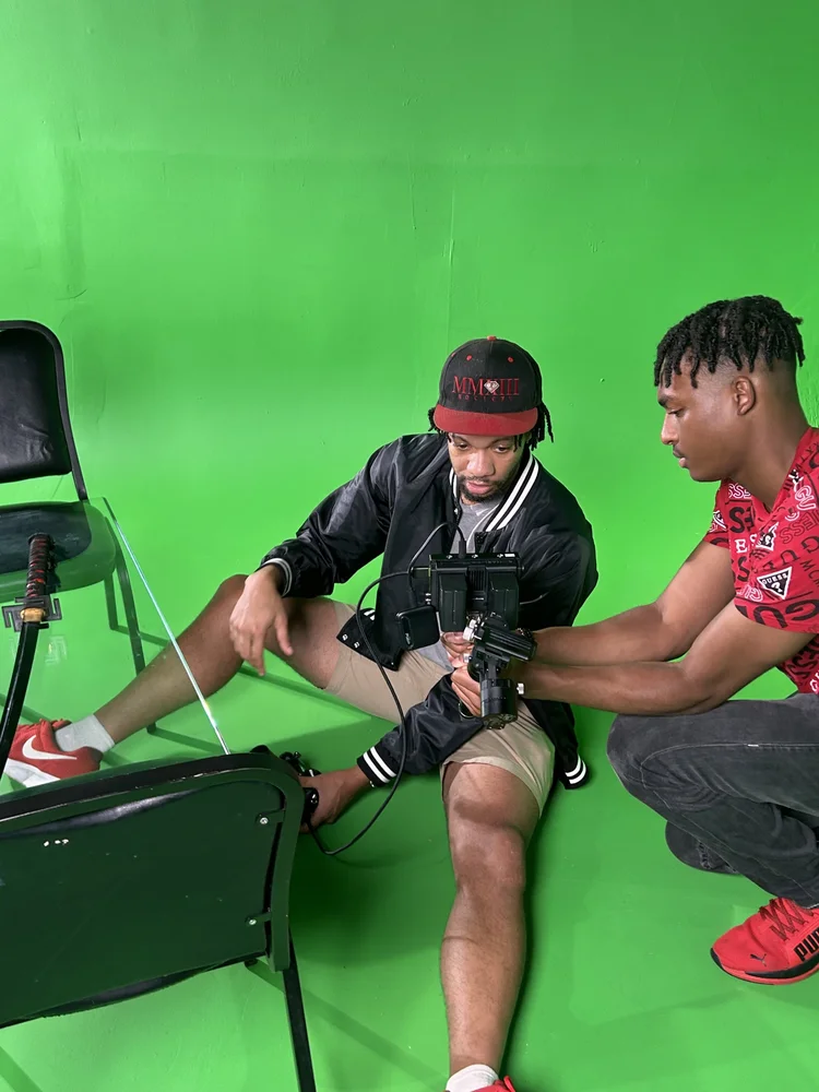 Crew member setting up a camera with talent on a green-screen set