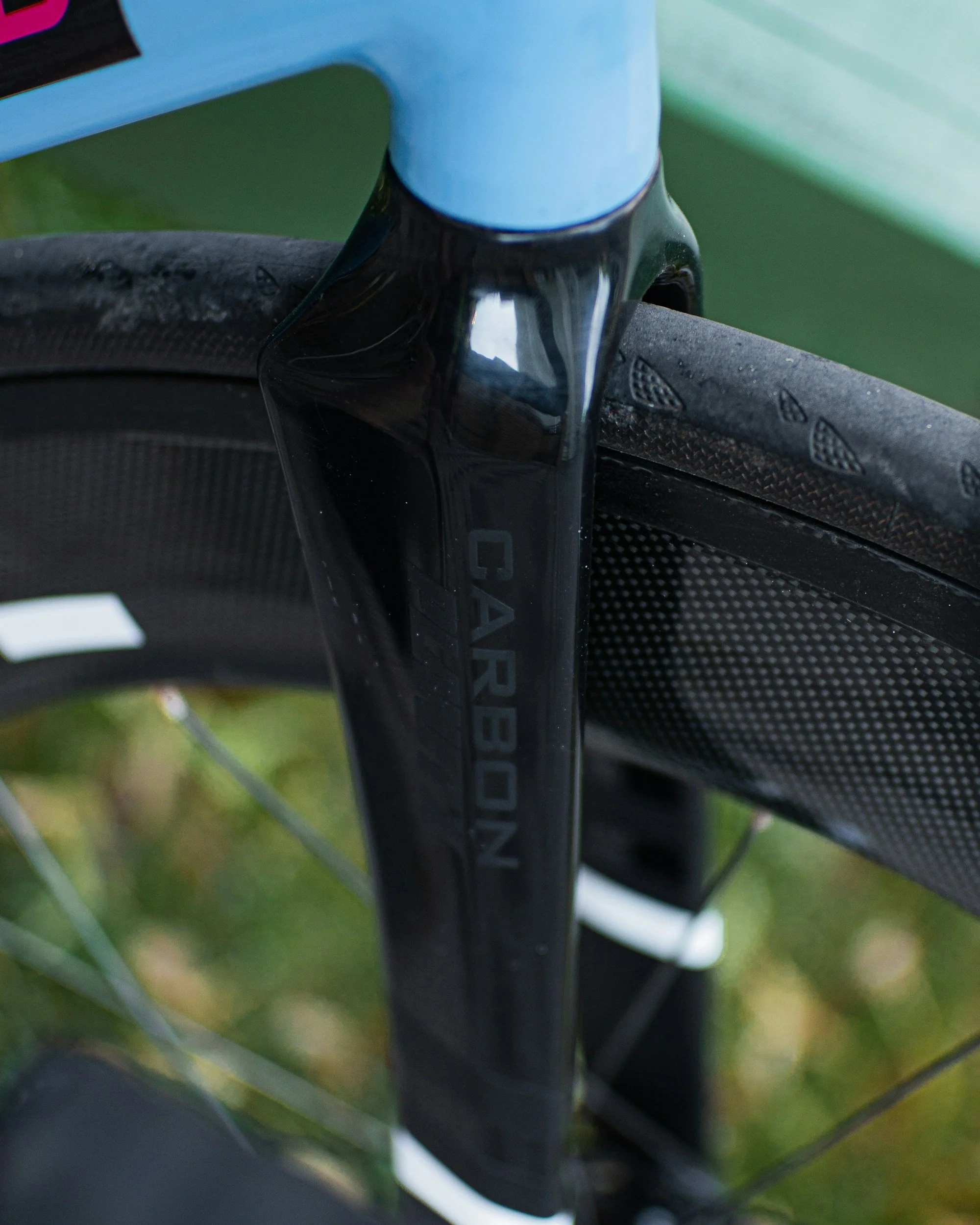 Close-up of a carbon fiber bicycle fork with the brand name 'CARBON' visible, attached to a black and blue bicycle frame.