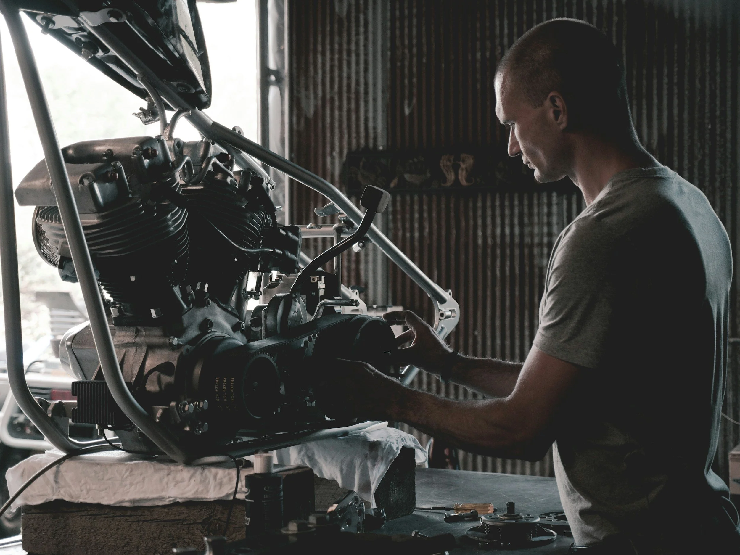 A man working on a motorcycle engine in a garage or workshop, with tools and parts on the workbench.