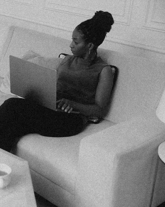 A woman sitting on a white sofa, using a laptop in a room with paneled walls.