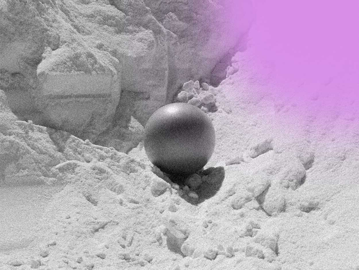 Black sphere resting on a snowy surface with a snow-covered rocky background and a purple light gradient in the top right corner.