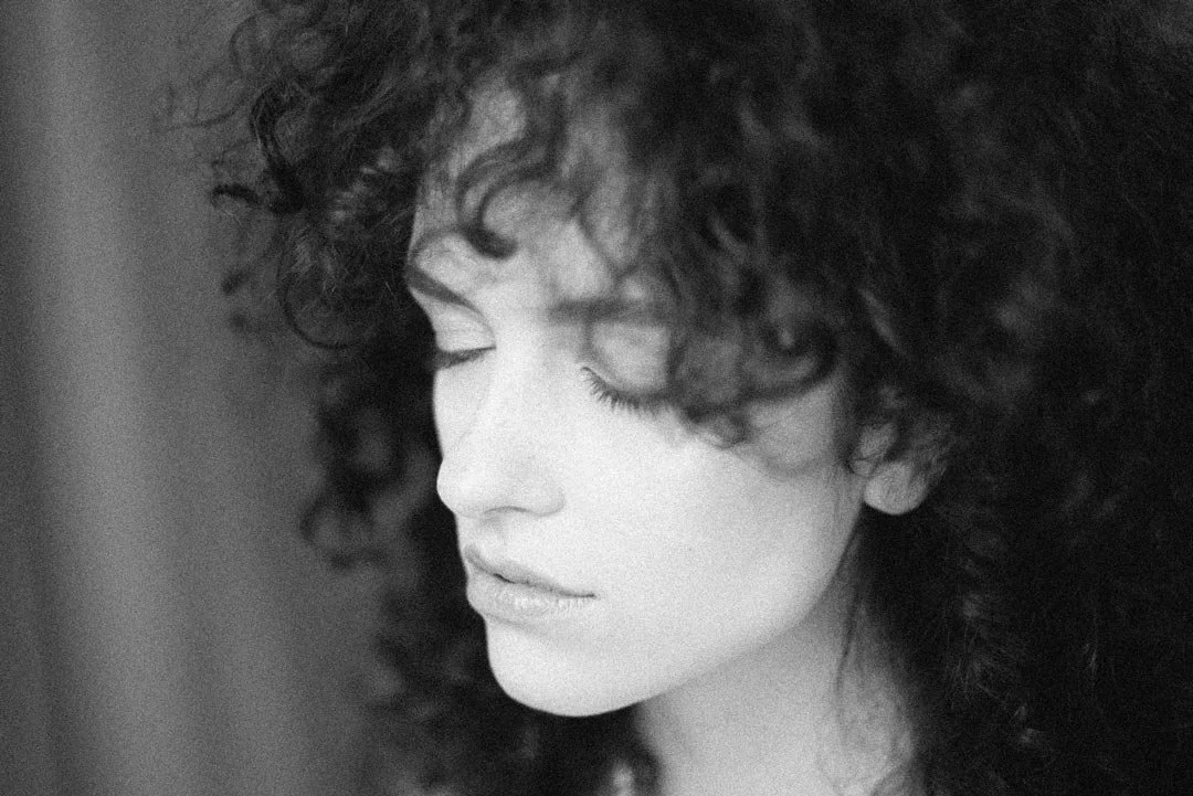 Close-up black and white photo of a woman with curly hair, eyes closed, peaceful expression.