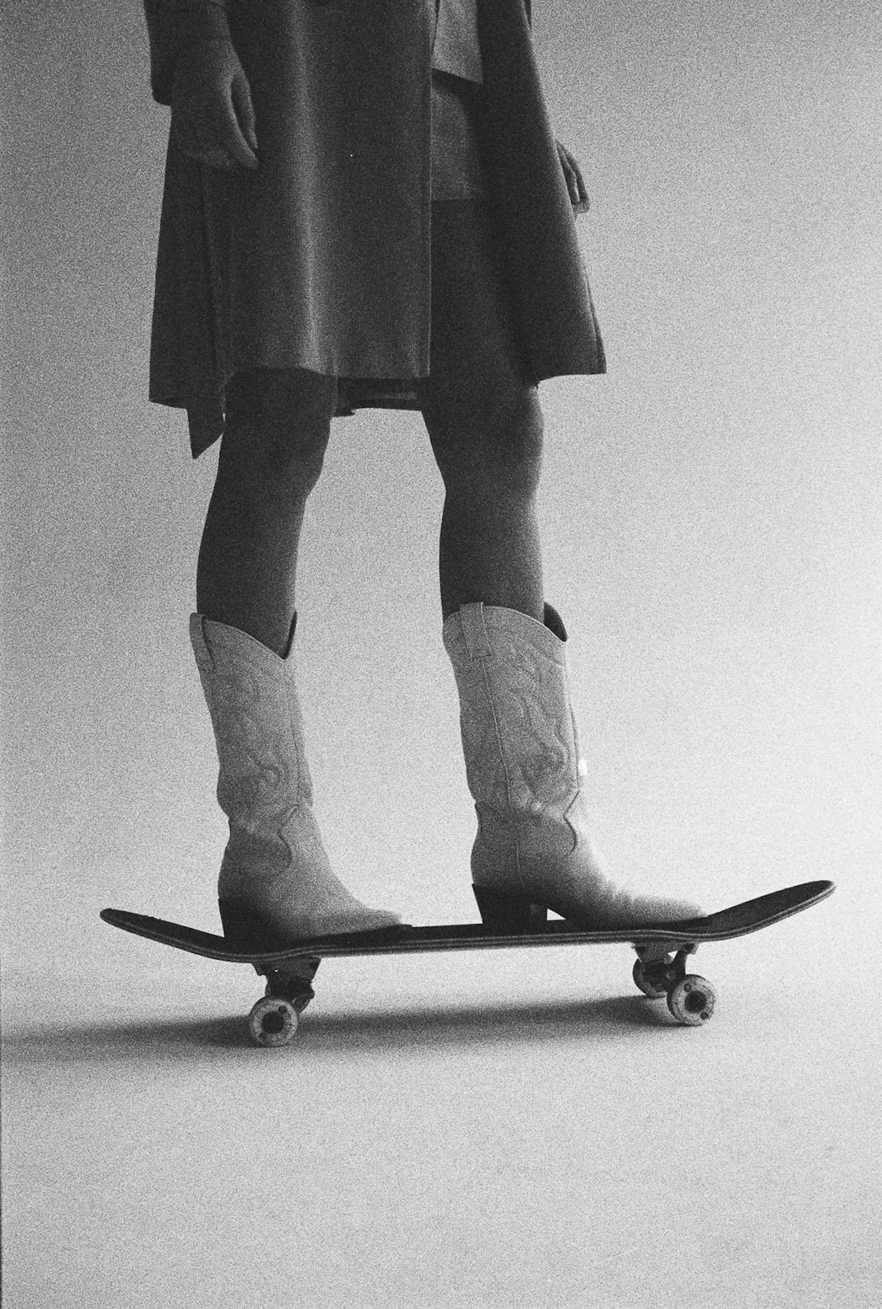 Person wearing cowboy boots and shorts standing on a skateboard.