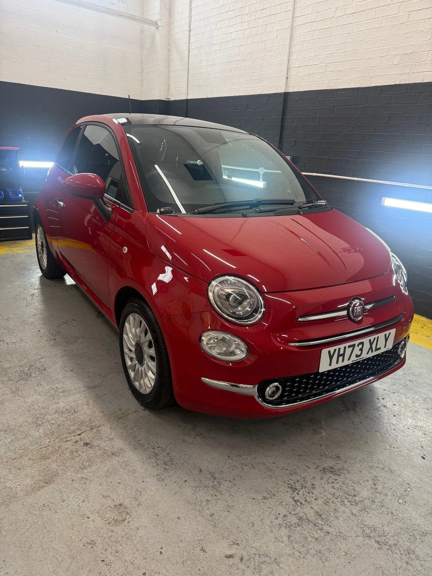 Red Fiat 500 compact car parked inside a garage with black and white walls and fluorescent lighting.