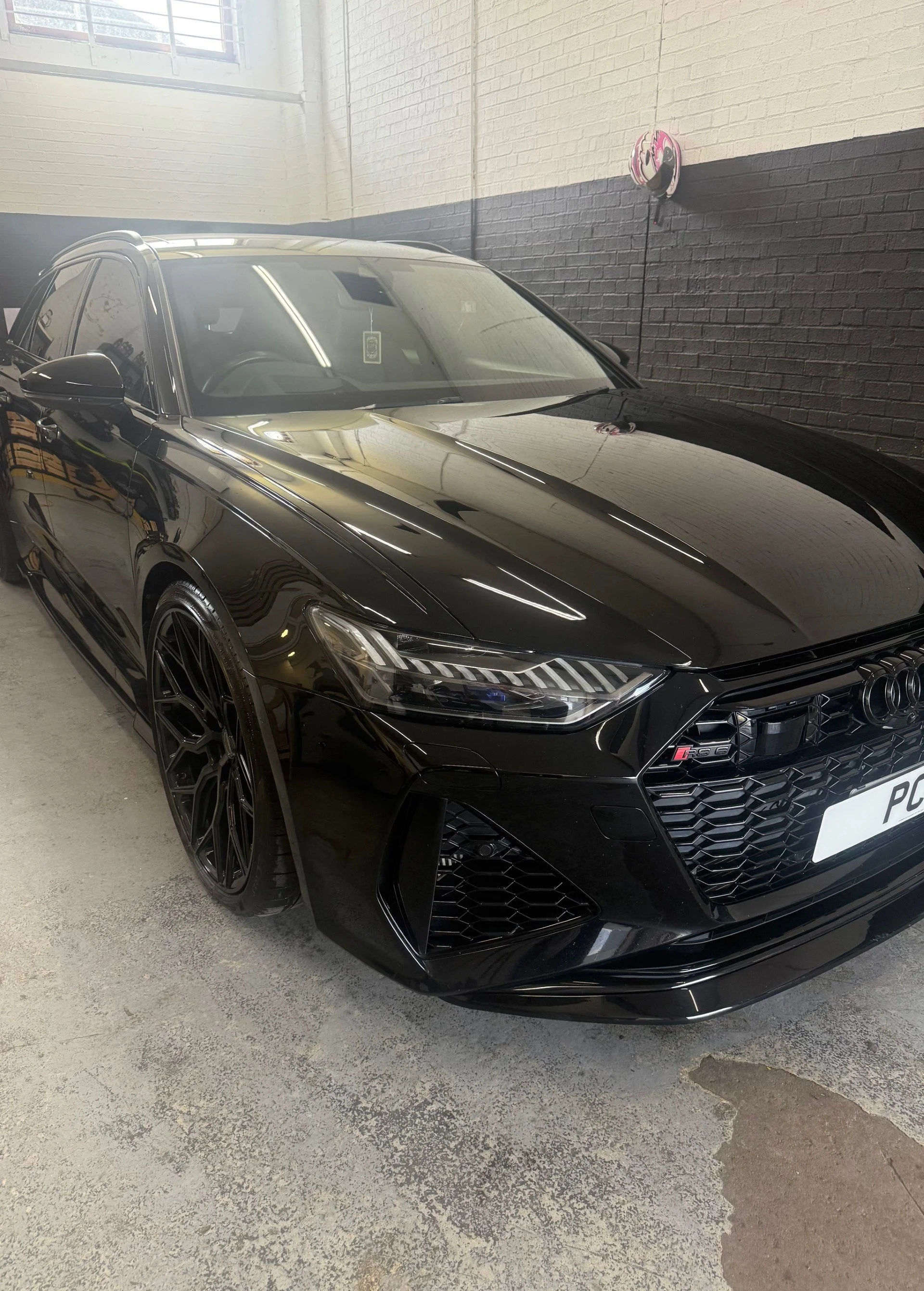 Black Audi RS5 parked indoors, with a garage wall in the background and overhead lighting reflecting off the car's surface.