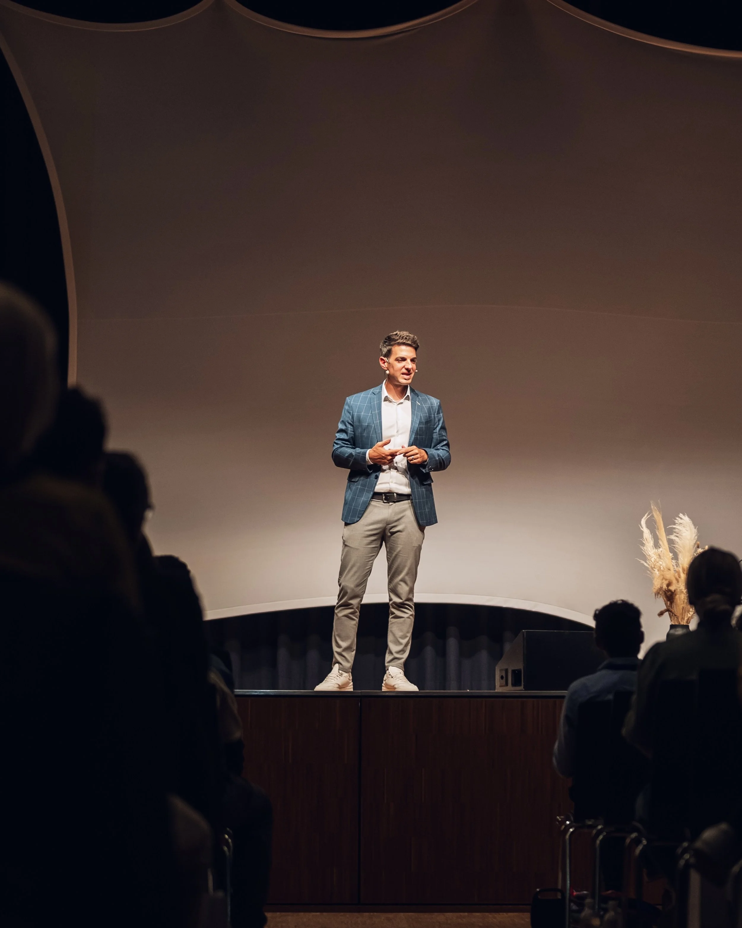 Mann hält Vortrag auf Bühne vor Publikum in dunklem Saal