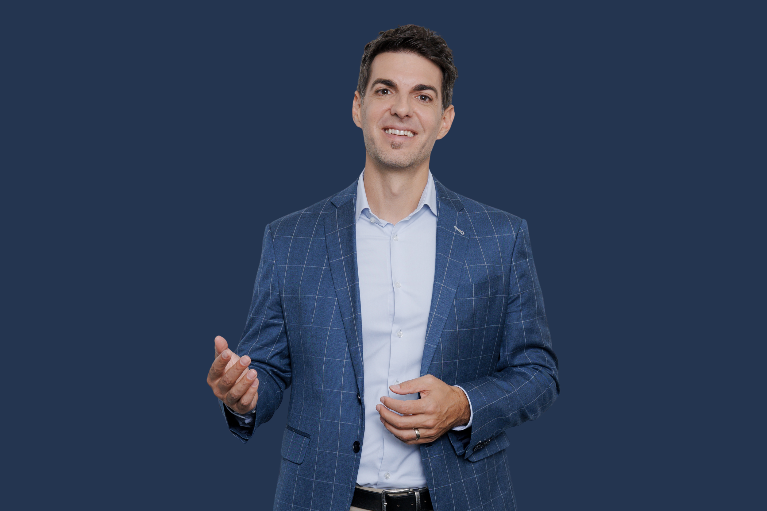 Ein Mann in einem blauen Anzug mit dezentem Karo-Muster, weißen Hemd und dunkler Hose, der lächelnd vor einem dunklen Hintergrund steht.