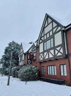 Snow-covered Tudor-style building with black and white timber framing and brick lower walls, surrounded by snow and trees.
