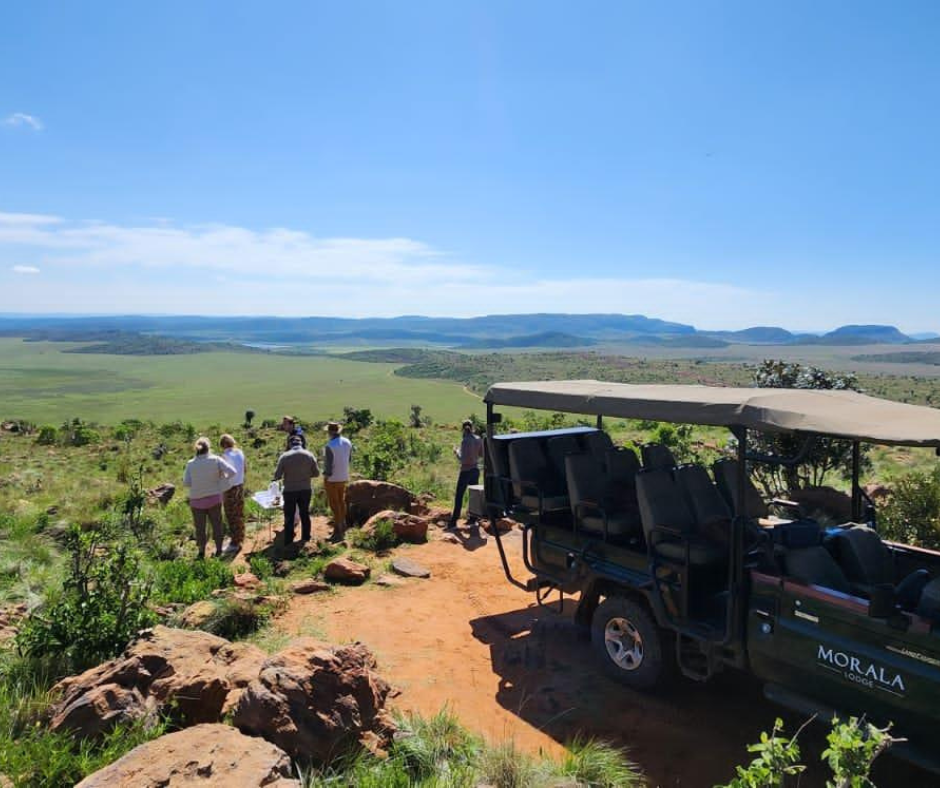 Group of people observing the landscape from a hilltop with a golf cart nearby on a bright, sunny day.
