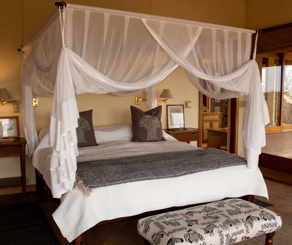 A bedroom with a four-poster bed featuring sheer canopy drapes, decorative pillows with tree patterns, and a bench with zebra print at the foot of the bed.