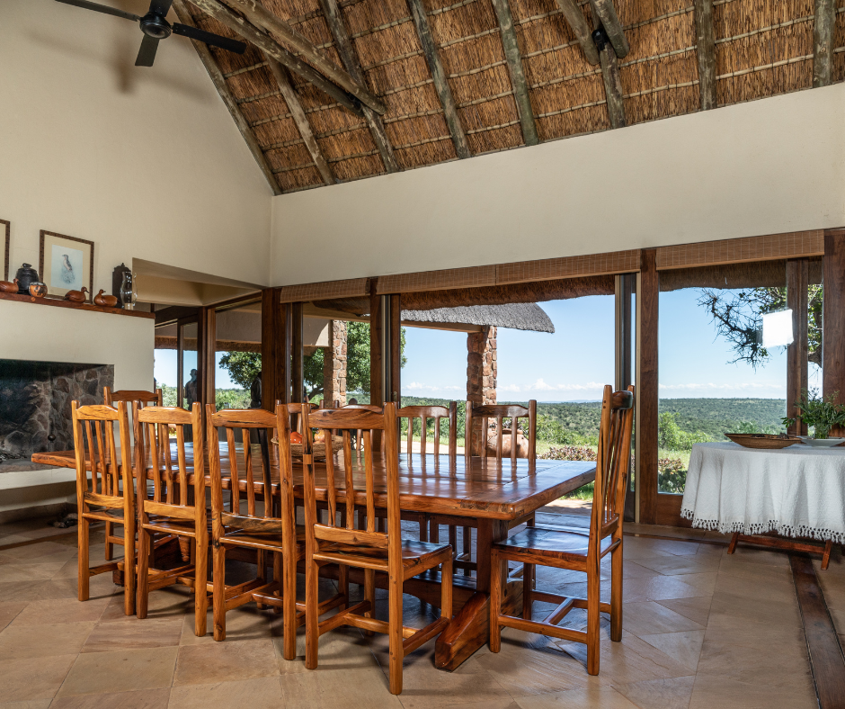 Dining room with wooden table and chairs, large windows with outdoor view, fireplace, and decorated mantel.