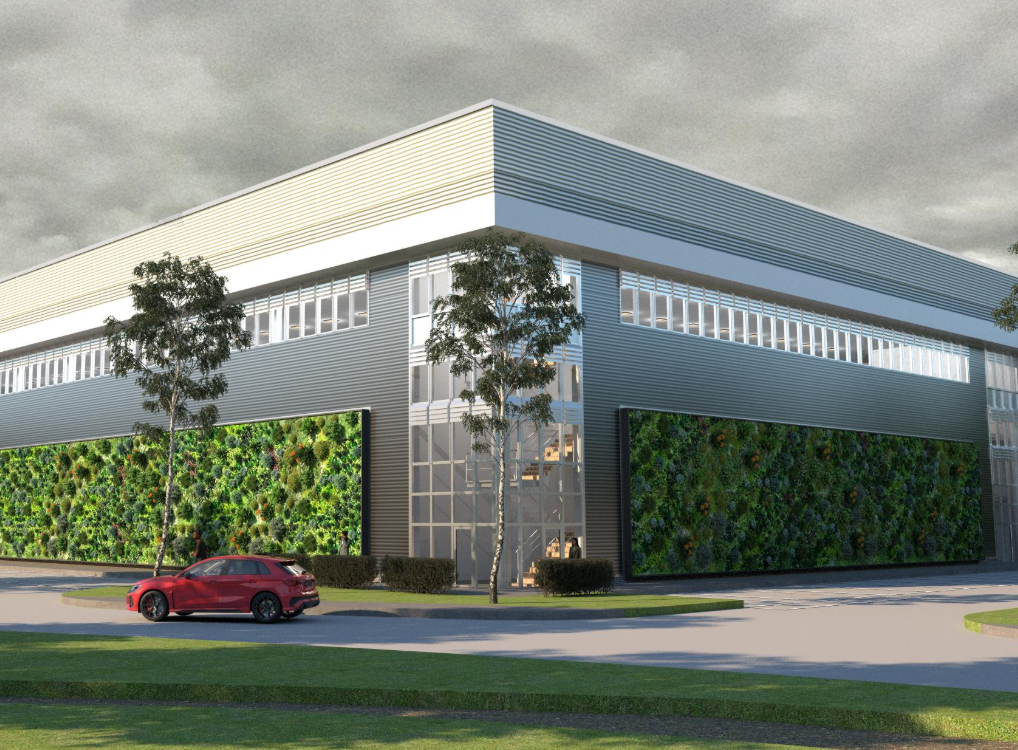 Modern commercial building with metal siding, large windows, and green vertical gardens on the walls, surrounded by trees and a parking lot with a red car, under a cloudy sky.