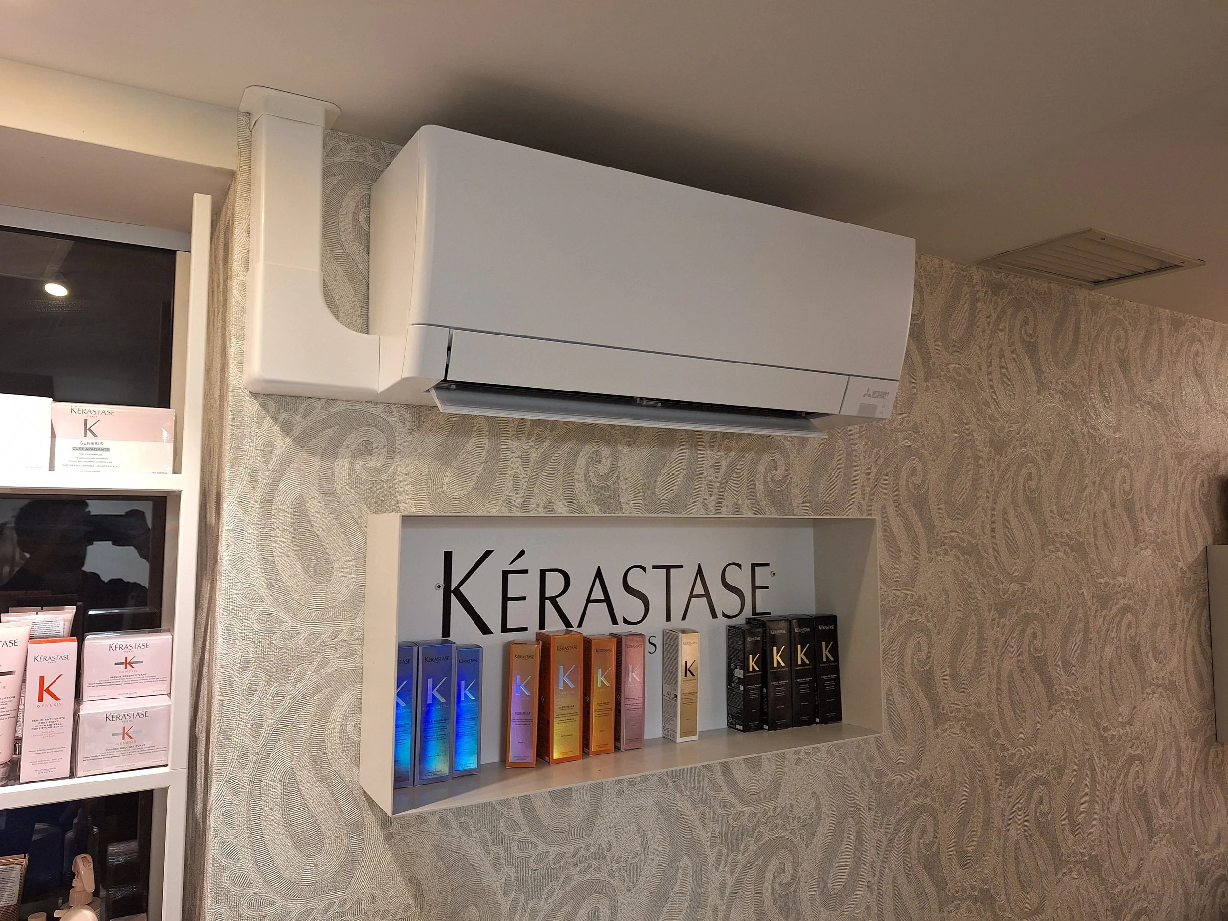 Streha z HVAC napravo, dvema črnima prezračevalnima odprtinama in sosednjimi stavbami v ozadju.