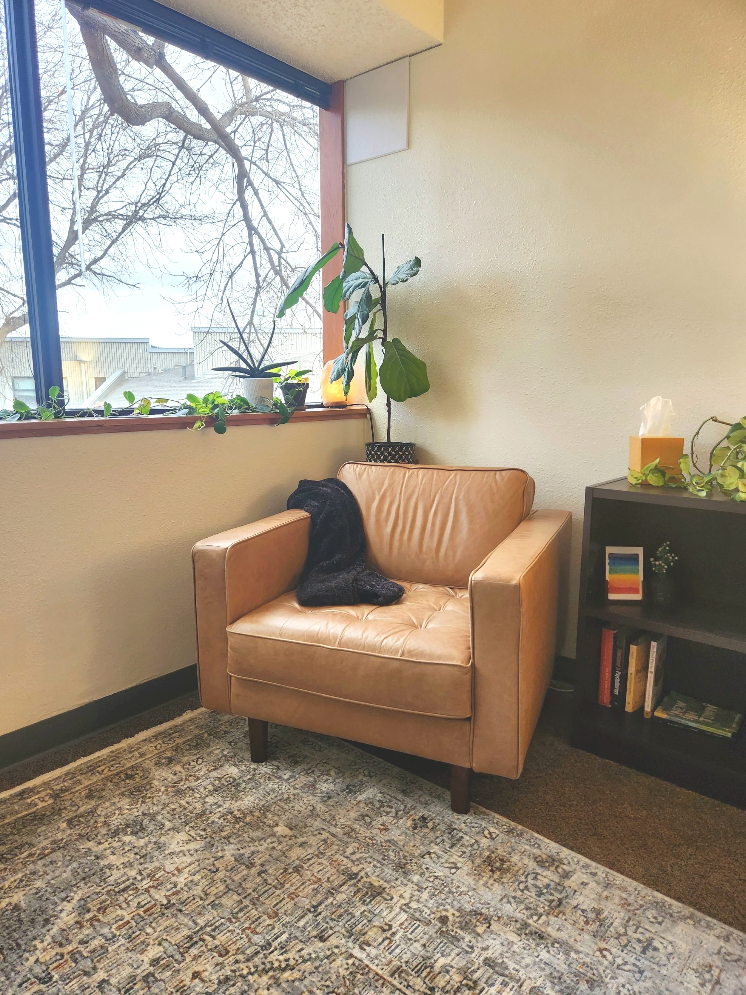 Warm and collaborative Fort Collins therapy office with cozy leather chair, natural light, and calming plants reflecting a relational, affirming counseling approach.