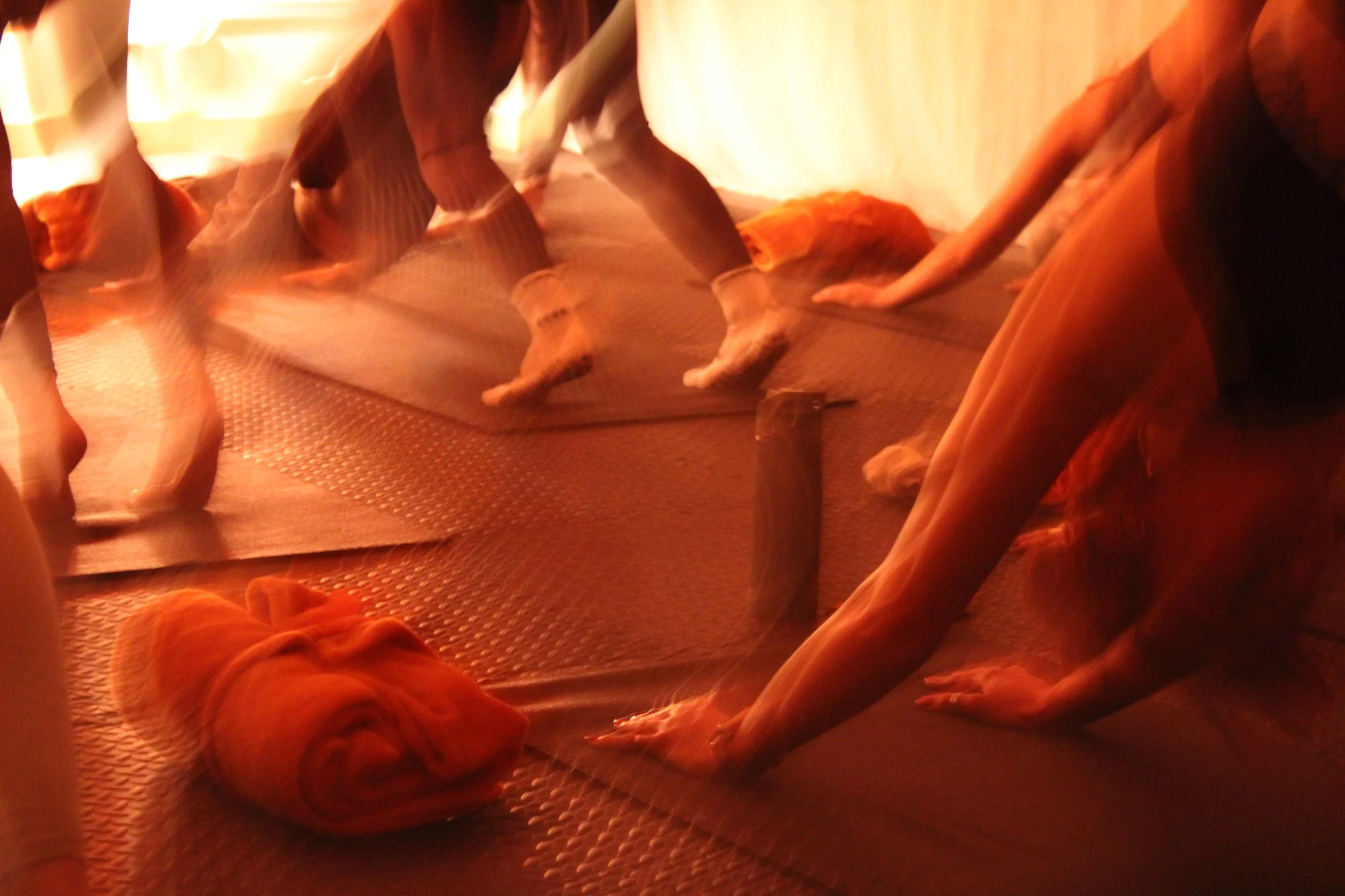 Group of people practicing yoga on mats in a dimly lit room, doing downward dog pose.