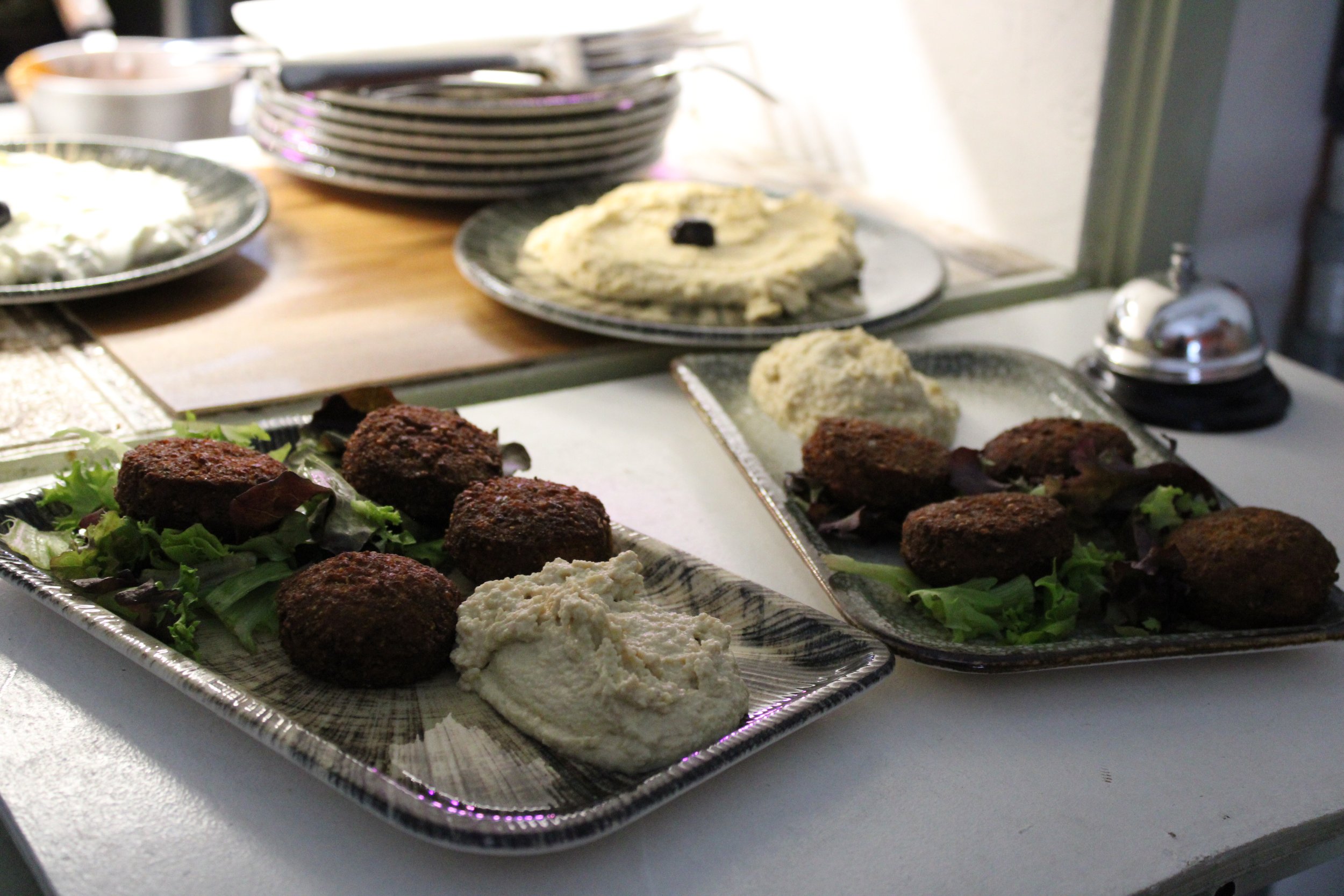 Platters of falafel balls with hummus and salad greens, with additional plates of dips and side dishes in the background.