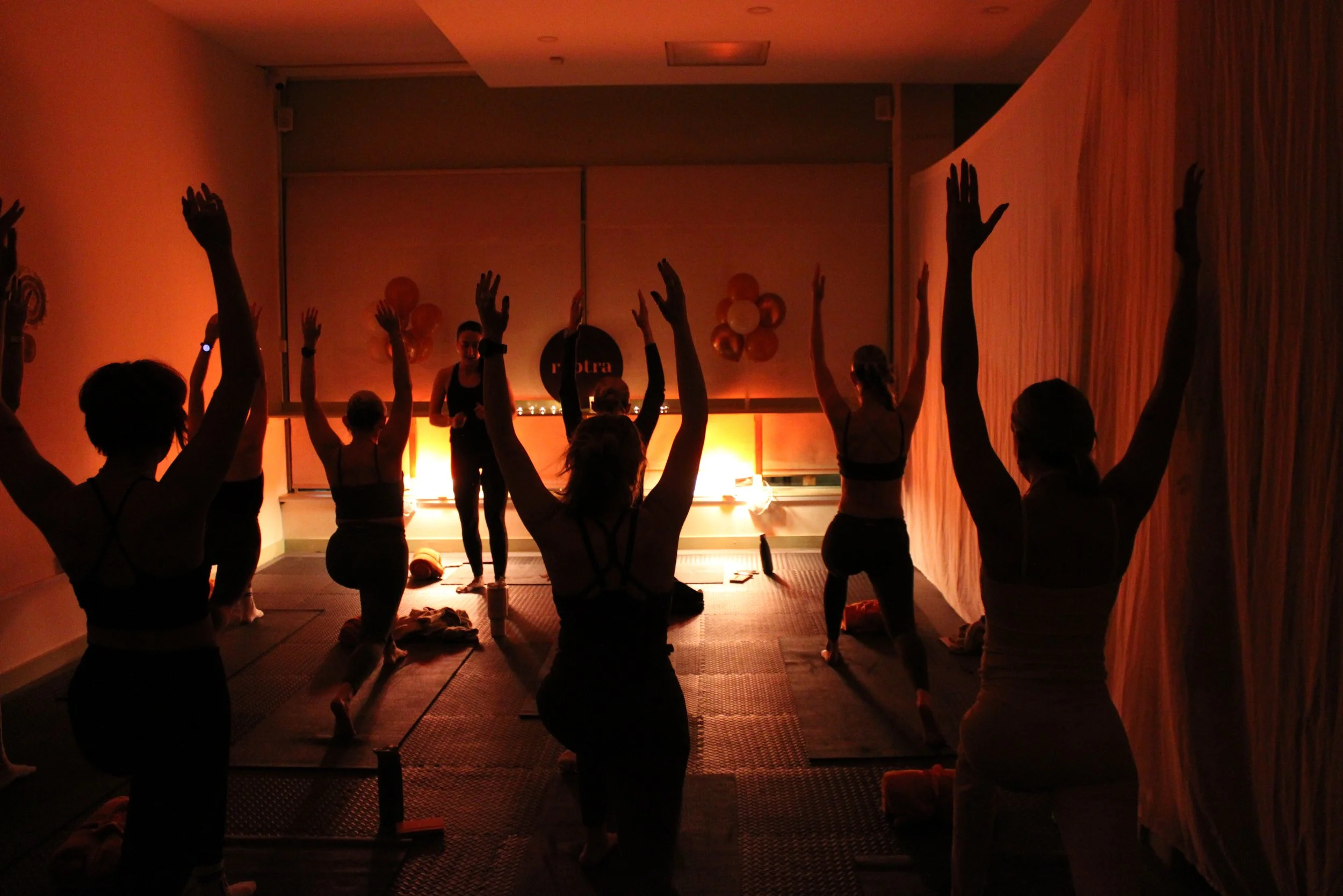 People attending a yoga class in a dimly lit room with orange lighting, practicing yoga poses on mats.
