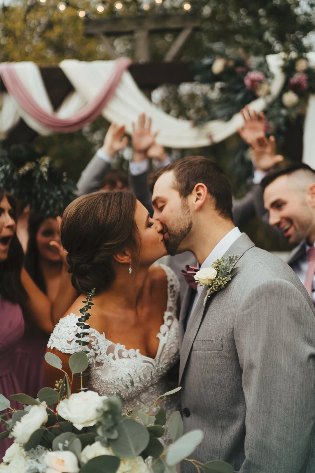 A bride and groom sharing a kiss during an outdoor wedding ceremony, surrounded by celebration guests and decorated with floral arrangements | Videography and Photography | Evansville, IN