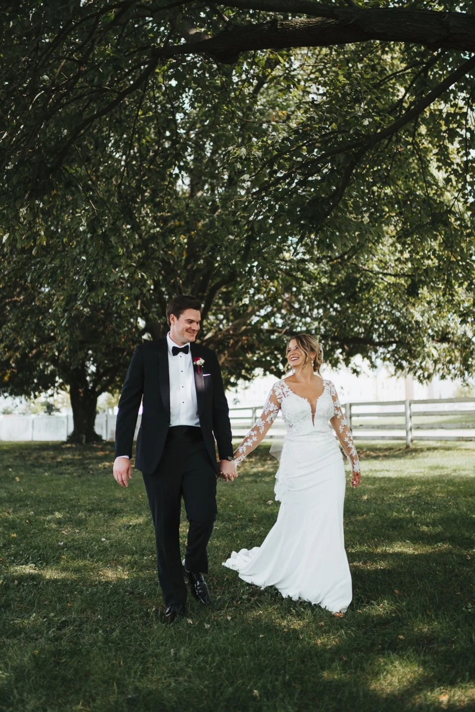 A bride and groom holding hands and walking outdoors, smiling on their wedding day | Videography and Photography | Evansville, IN