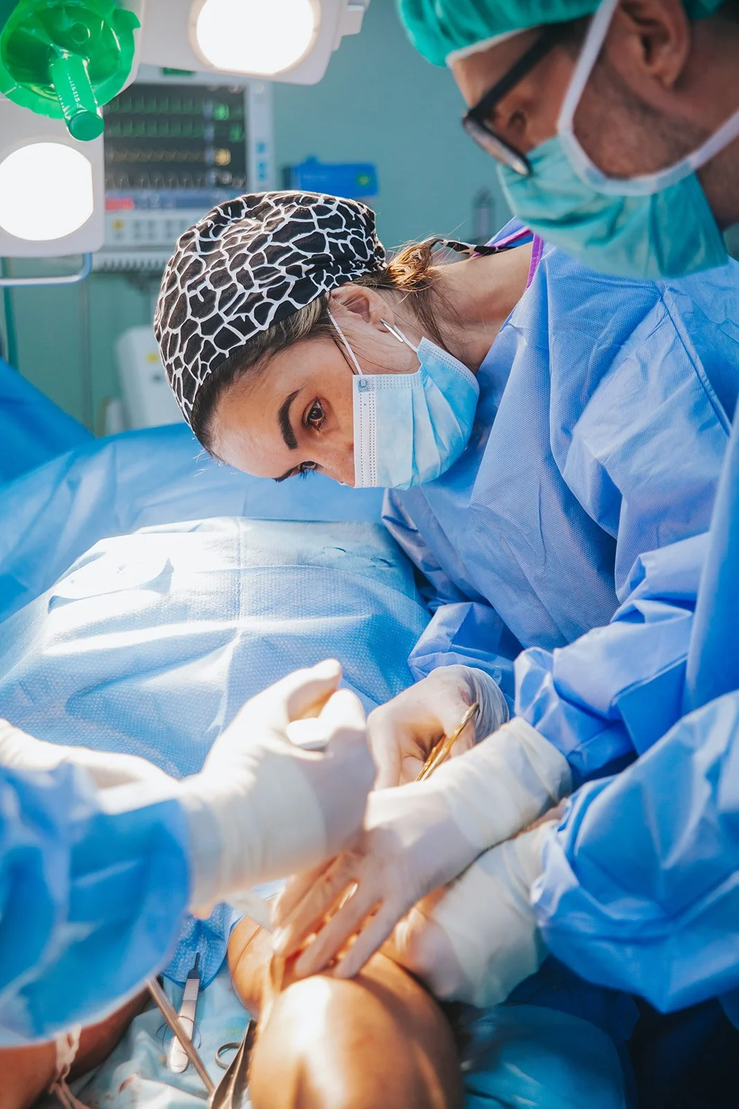 Equipe de cirurgiões realizando uma cirurgia em um paciente, usando aventais azuis, máscara e luvas cirúrgicas.