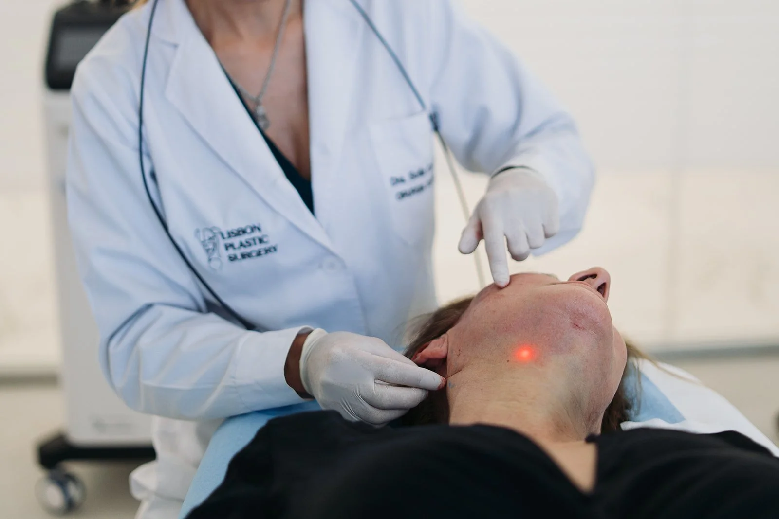 Médico realizando procedimento médico na garganta de um paciente, usando luvas e um aparelho de luz vermelha.