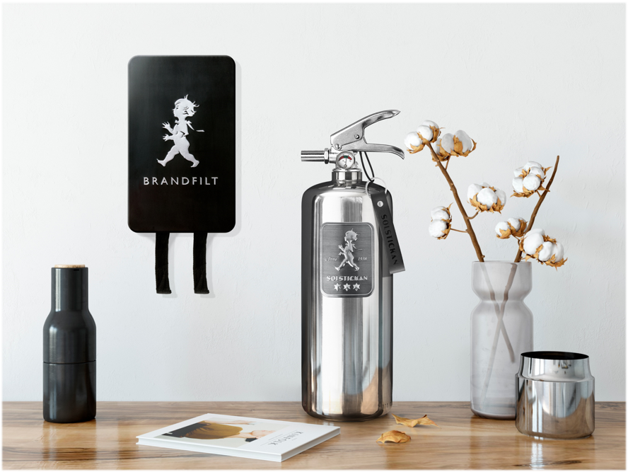 A stylish interior display including a black wall-mounted object with the word 'BRANDFIT' and a cartoon figure, a metallic fire extinguisher with a tag labeled 'SOTSICKAN,' a black and gold water bottle, a white book with an image of a coffee cup, a clear glass vase with cotton branches, and a small metallic container, all on a wooden surface against a white wall.