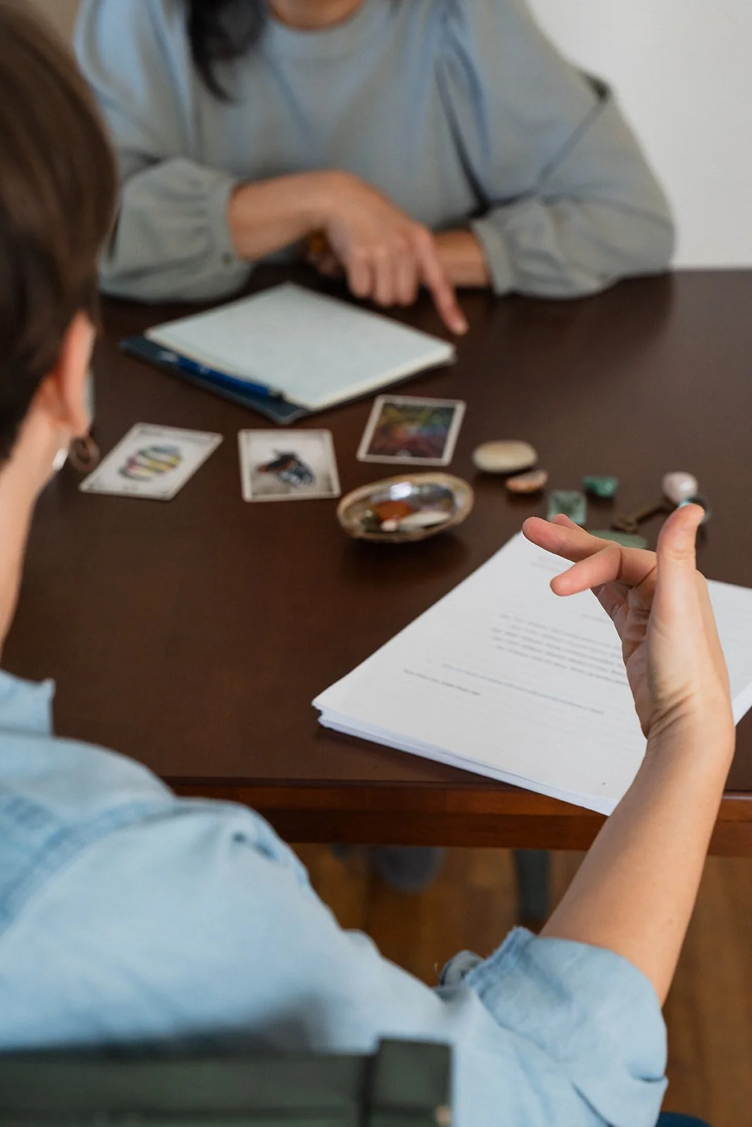 People having a tarot card reading with tarot cards, a notepad, and stones on the table.