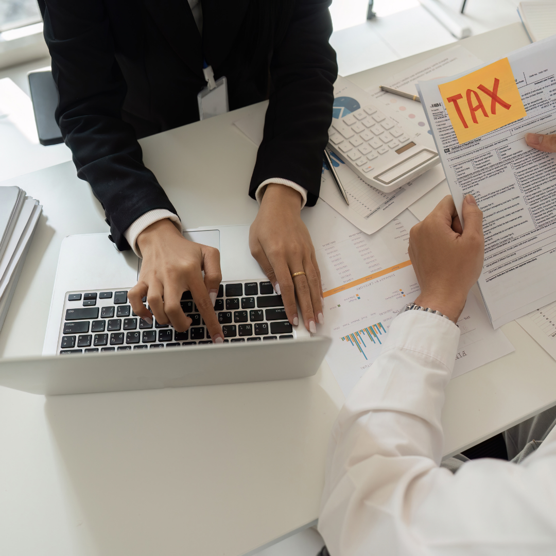 People working on tax documents with a sticky note labeled 'TAX' in an office.