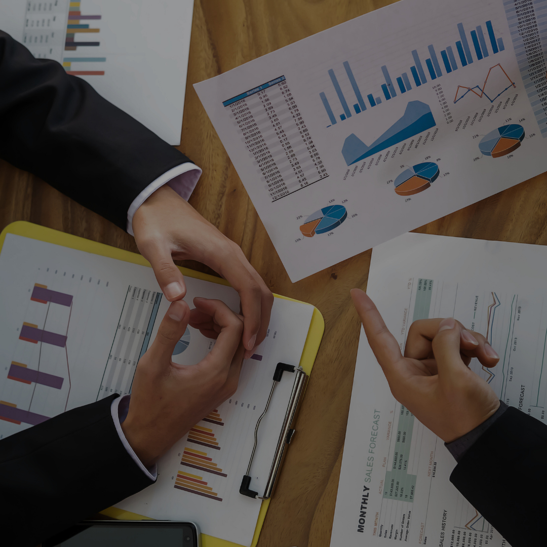 Two people discussing business reports and charts on a wooden table, including bar graphs, pie charts, and line graphs.