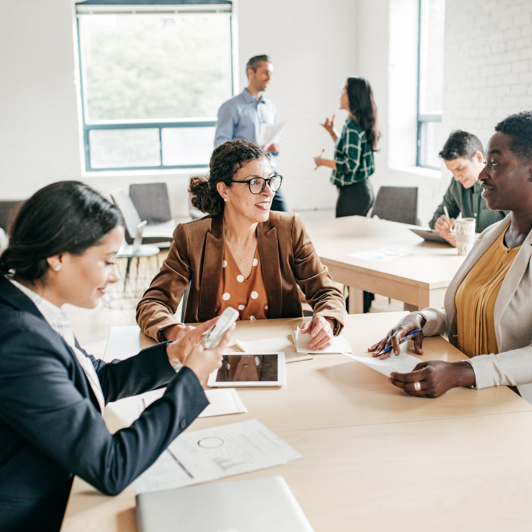 People having a business meeting in a modern office with large windows, focused on a woman using a smartphone.