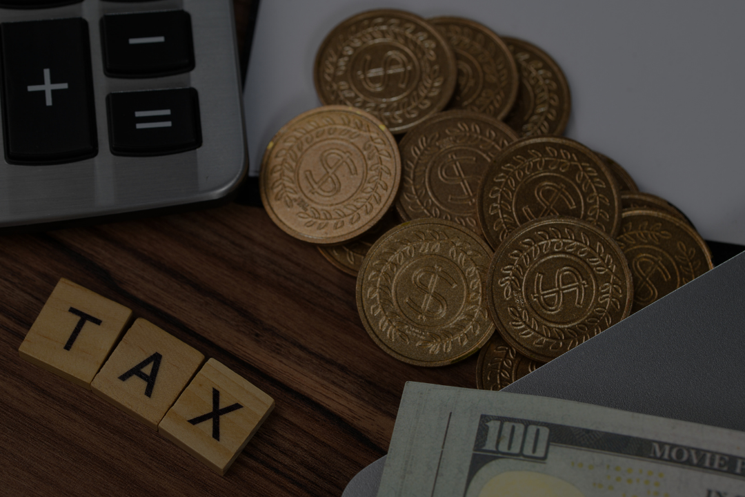 Decorative fake gold coins, a calculator, a few euro banknotes, and wooden blocks spelling 'TAX' on a wooden surface.