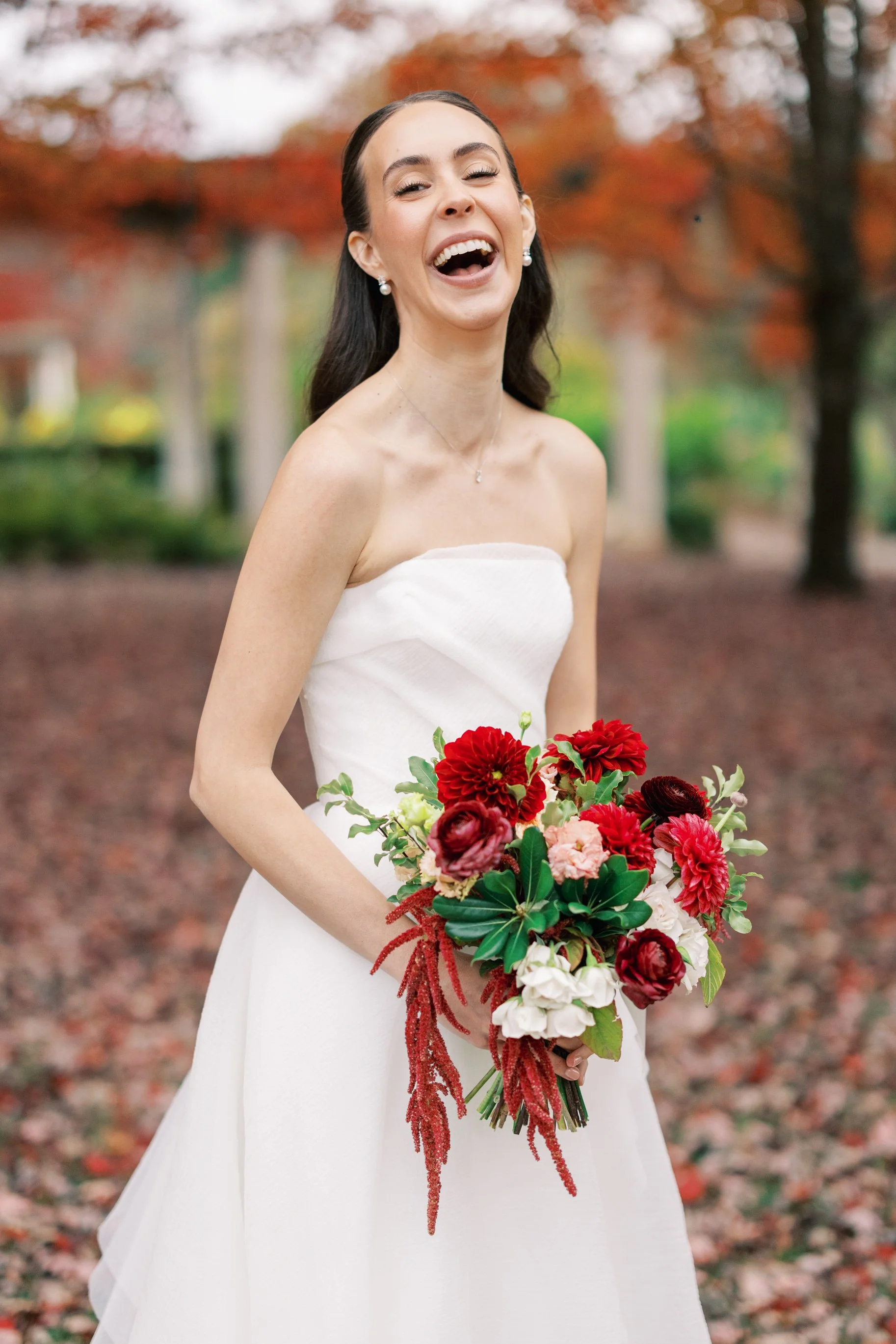 A woman in a white dress with brown hair holding a bouquet of red flowers after getting married. Bridal hair and makeup by professional makeup artist, Carly Amico of Carly Marie Artistry, a makeup artist in Charlotte NC.