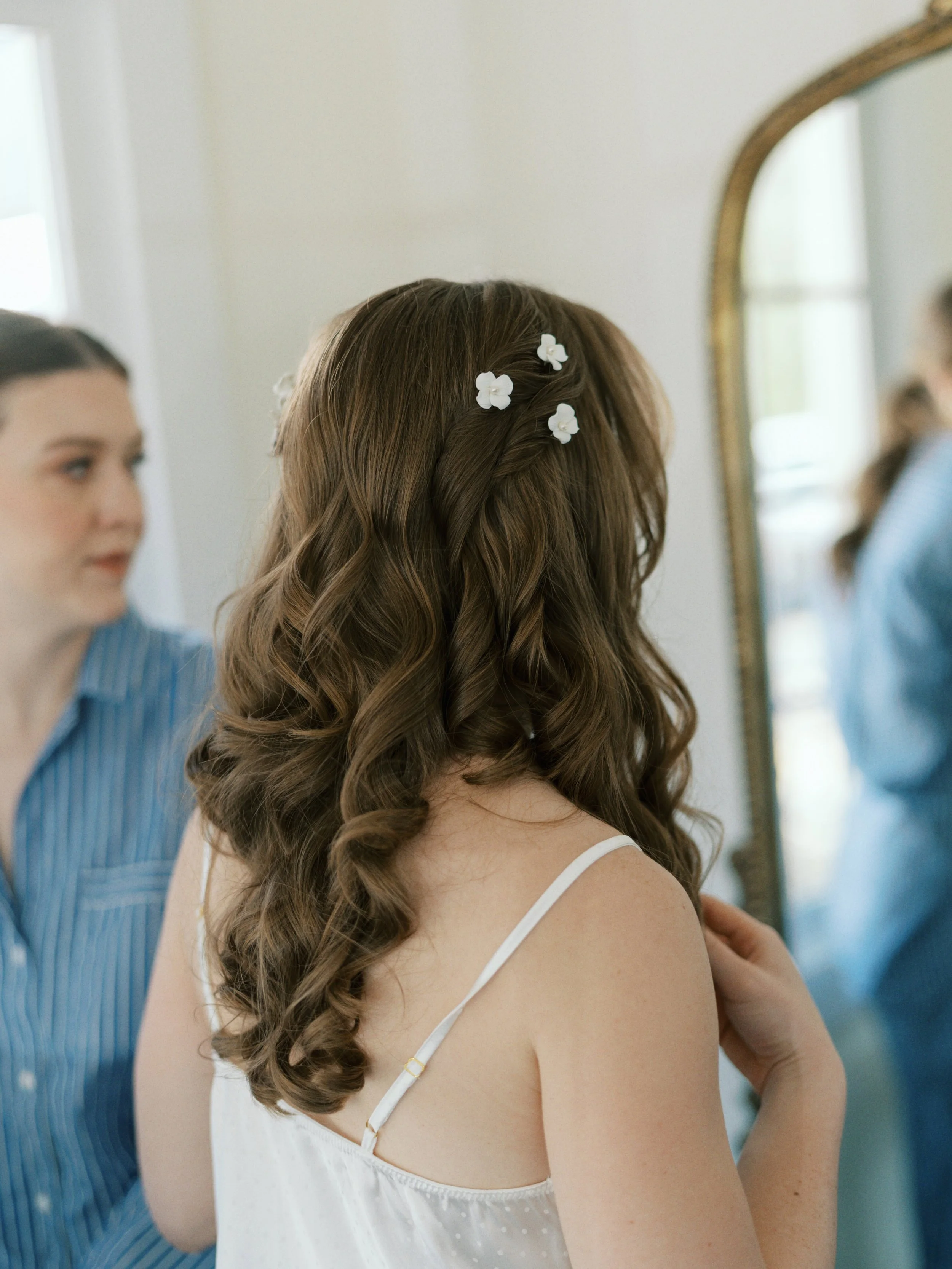 A woman with brown wavy hair looking at herself in the mirror while she waits to get married. Bridal hair and makeup by professional makeup artist, Carly Amico of Carly Marie Artistry, a makeup artist in Charlotte NC.