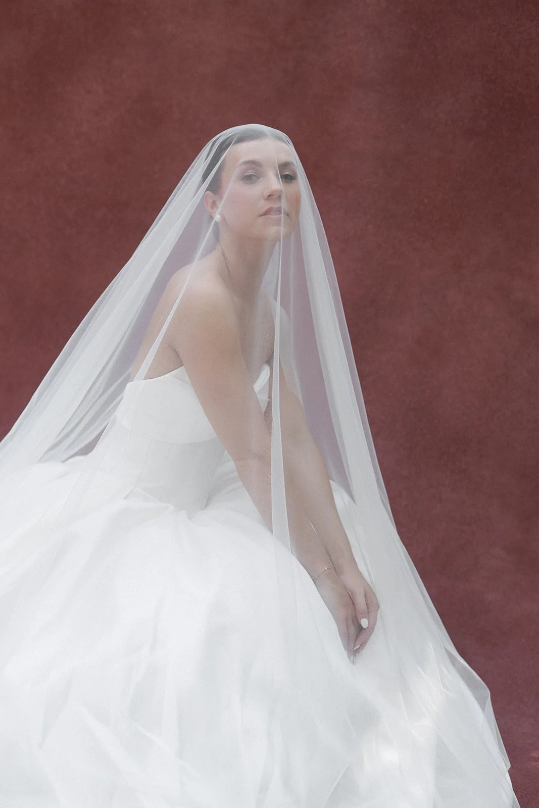 A woman is in a white wedding dress with a veil draped over her. She has a slick back bun bridal hairstyle and soft glam bridal makeup. The photo was taken in charlotte nc. Bridal hair and makeup by professional makeup artist, Carly Amico of Carly Ma
