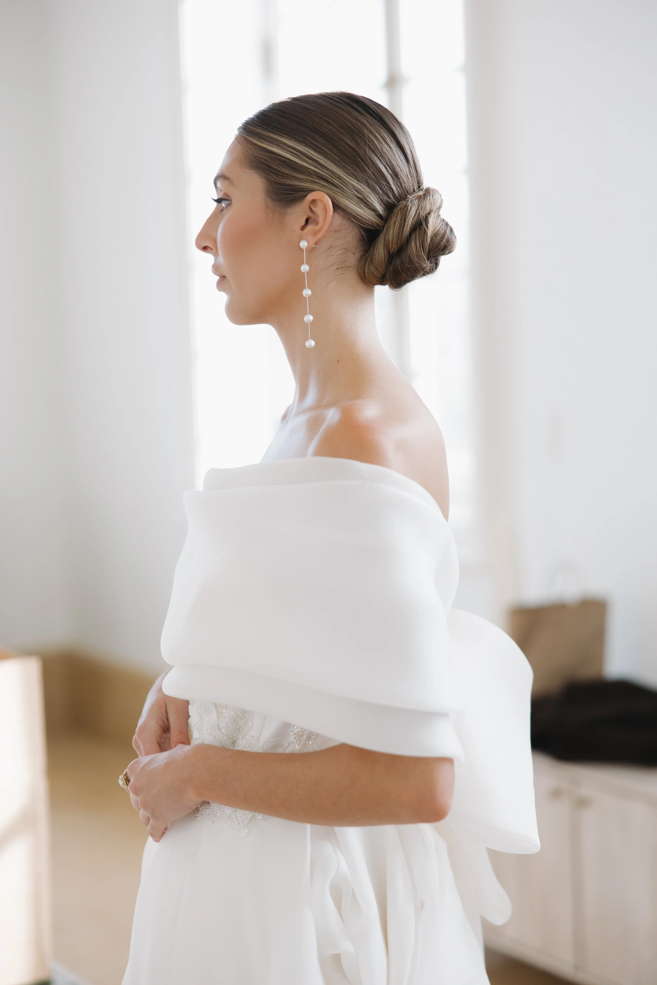 A women with brown and blonde hair in a white wedding dress poses for photos on her wedding day. She is wearing her hair in a slick back bun. Bridal hair and makeup by professional makeup artist, Carly Amico of Carly Marie Artistry, a makeup artist i