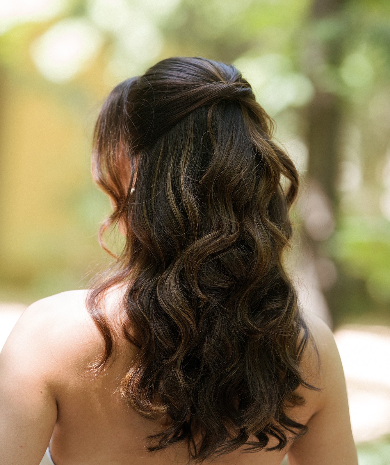 A woman in a white wedding dress is posing for a photo. She is wearing her hair in a half up half down with voluminous curls and face framing. Bridal hair and makeup by professional makeup artist, Carly Amico of Carly Marie Artistry, a makeup artist 